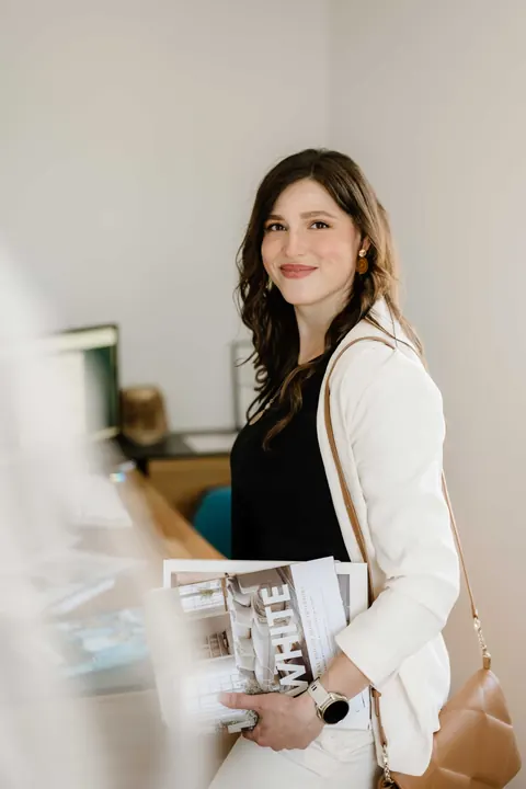 Kristina Haingartner lächelnd mit Einrichtungsmagazinen in ihrem Büro